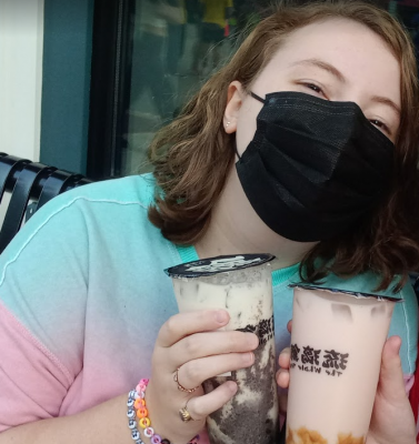 A white person with brown eyes and blonde hair looking at the camera and holding bubble tea.